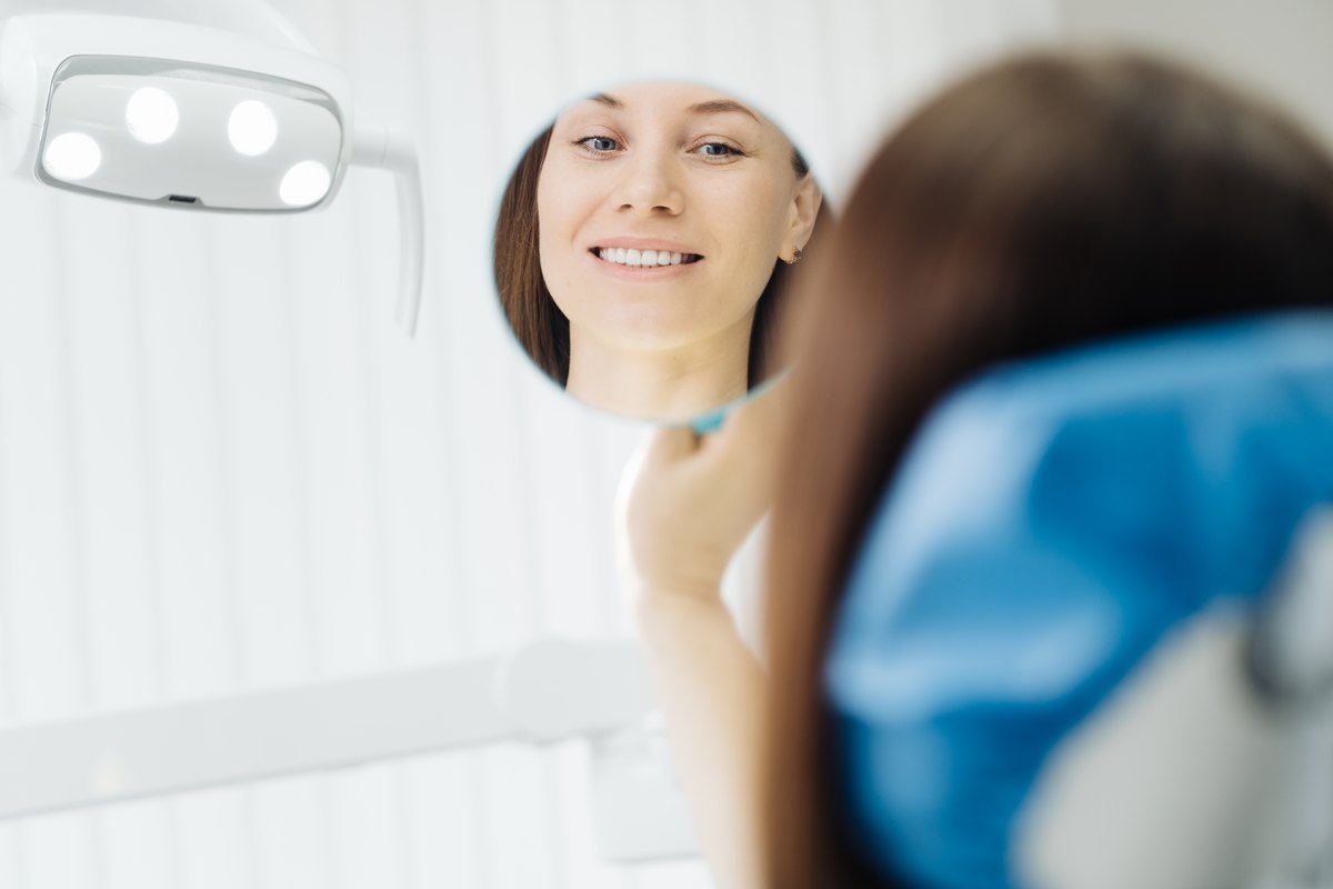 Smiling patient admiring her new smile in a hand mirror at Cagigas Dental in Lake Worth, FL